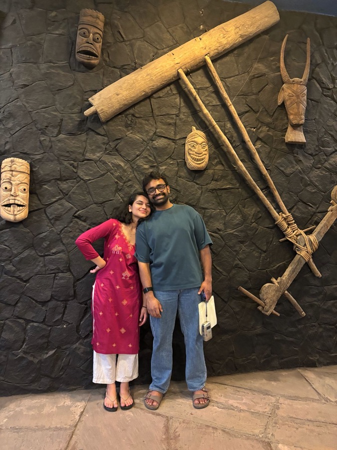 Aaditya and Gauri in front of a wall of carved masks